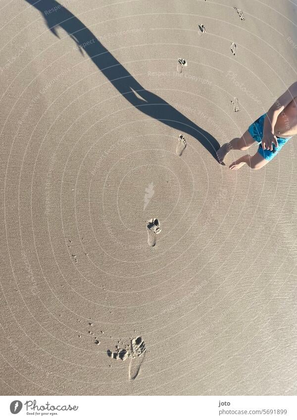 Kinder hinterlässt am Strand Fußspuren und bildet einen Schatten Fußgänger Fußspuren im Sand Sandstrand Nordseeküste Schattenwurf Schattenbild Badebekleidung