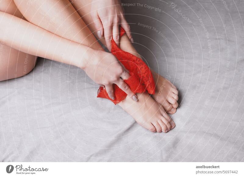 Beine einer Frau, die sich im Bett auszieht und ihr rotes Spitzenhöschen bis zu den Füßen herunterzieht Frauenunterhose Fuß Ausziehen ziehend nach unten