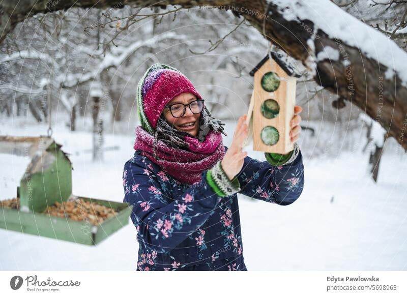 Frau legt Vogelsamen in Vogelfutterhaus im Winter füttern Korn Vögel Futterhäuschen Zuführung Schnee kalte Temperatur Wetter Freizeitaktivitäten Lebensstile