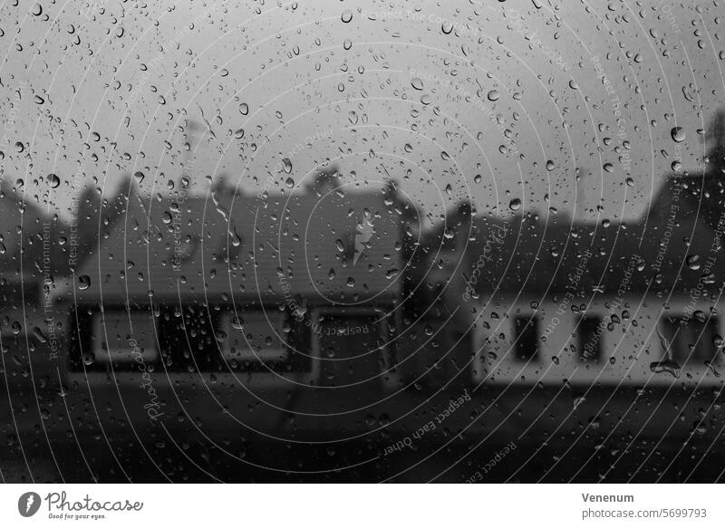 Schwarzweißfoto, Häuser hinter einer Fensterscheibe mit vielen Regentropfen schwarzweiß Schwarzweißfotografie Schwarzweißaufnahme Regenwetter Haus Photographie