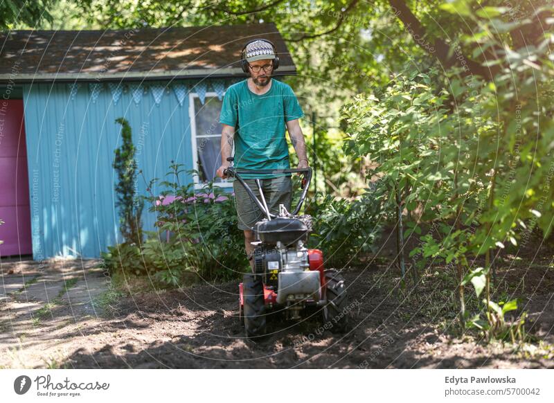 Mann arbeitet mit Motorkultivator in seinem Gemüsegarten ROTOVATOR Kultivator Gartengeräte Freizeitaktivitäten Lebensstile Gartenarbeit Aktivität Tag im Freien