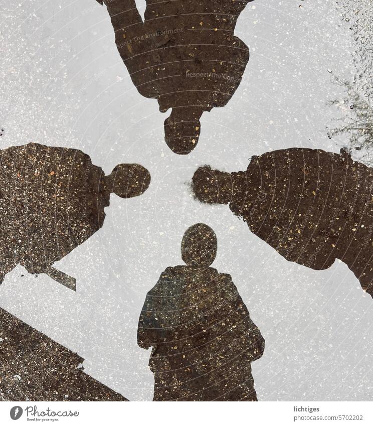 Vierfalt- Schatten von vier Menschen in einer Pfütze regen spiegelung menschen spiel kontrast