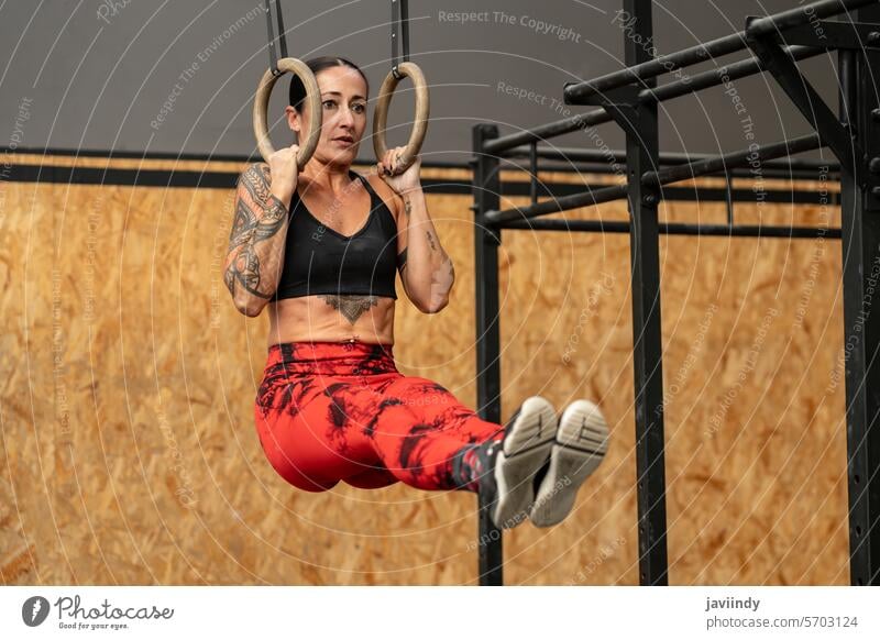 Frau führt Kernübungen an olympischen Ringen hängend aus Core-Übungen erhängen olympische Ringe Cross-Training Fitnessstudio Stärke sportlich Suspension