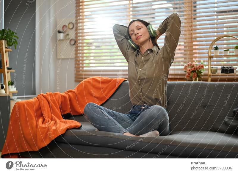 Glückliche junge Frau hört Lieblingsmusik mit Kopfhörern und entspannt sich auf der Couch zu Hause hören Musik Erholung Technik & Technologie Liege Sofa