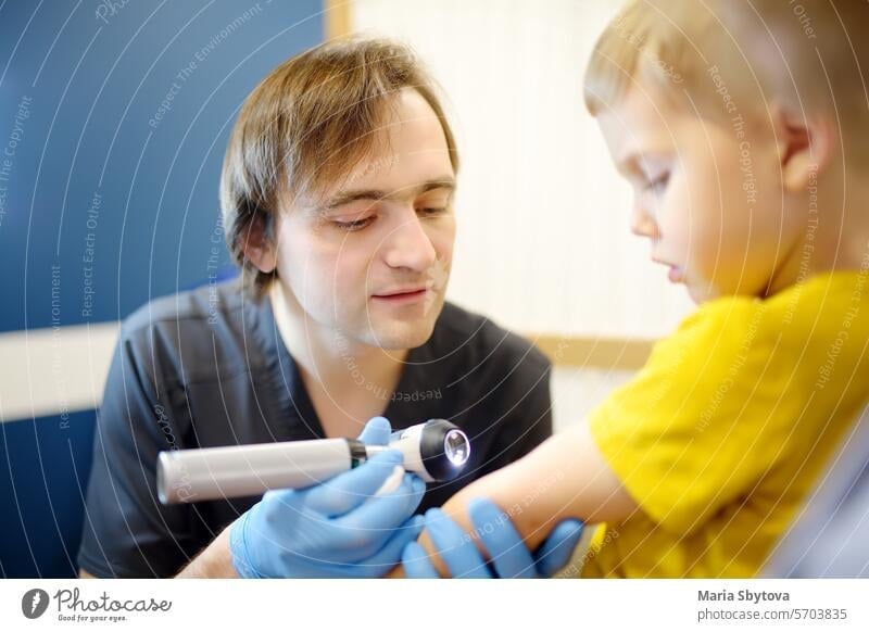 Ein fürsorglicher Arzt untersucht Muttermale auf der Haut eines Kleinkindes. Ein Dermatologe untersucht mit einem Dermatoskop einen Ausschlag an der Innenseite der Ellenbeuge eines Jungen.