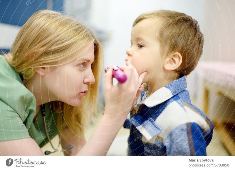 Ein süßes Kleinkind hat einen Termin bei einem fürsorglichen Kinderarzt. Der HNO-Arzt untersucht den Hals eines kleinen Patienten mit Blitzlicht. Kinderärztin