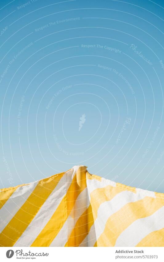 Gelb-weiß gestreifter Sonnenschirm vor klarem Himmel gelb Streifen übersichtlich blau minimalistisch Sommer Erholung Kontrast pulsierend Farbe Freizeit Urlaub