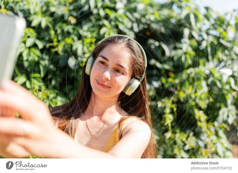 Junge Frau macht Selfie mit Smartphone im Freien jung Musik Kopfhörer Garten sonnig Technik & Technologie Mobile Foto Lächeln Freizeit Fröhlichkeit Erholung