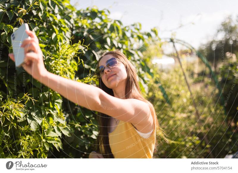 Frau nimmt Selfie in sonnigen grünen Garten Telefon Grün gelb Tanktop heiter jung üppig (Wuchs) Tag Smartphone im Freien Lifestyle Natur lässig Freizeit