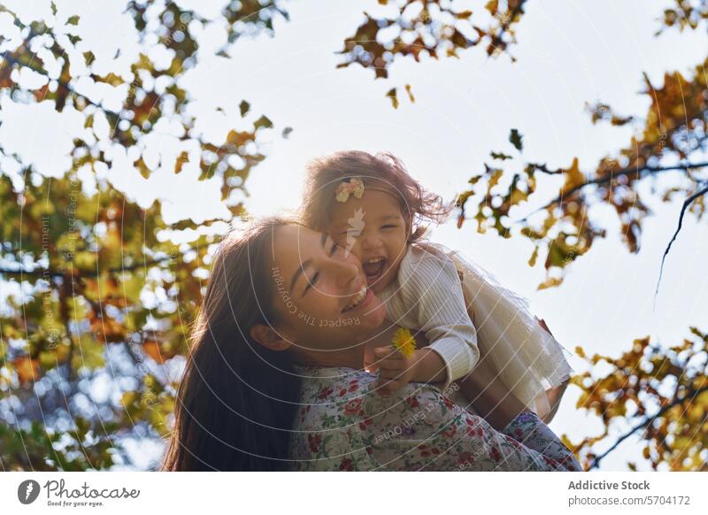 Niedriger Winkel pf fröhlichen ethnischen Mutter und Tochter in sonnigen Park Kalifornien USA Freude Liebe Herbst Blätter sonnenbeschienen Fröhlichkeit Familie