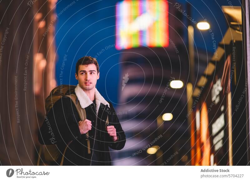 Junger Mann erkundet Madrid bei Nacht mit leuchtenden Neonschildern im Hintergrund jung erkundend neonfarbig Zeichen Illumination Rucksack urban Abenteuer