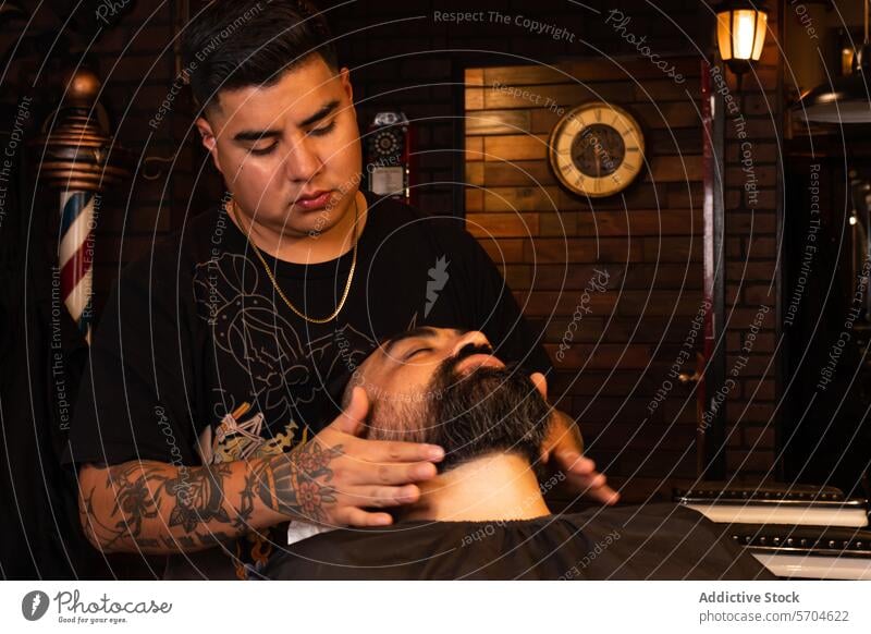 Konzentrierter Friseur, der den Bart eines Kunden im Friseursalon berührt Stylist berühren Vollbart Klient Barbershop Tattoo sich[Akk] entspannen Pflege