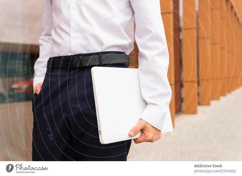 Nahaufnahme eines anonymen Mannes in weißem Hemd und marineblauer Hose, der einen Laptop hält, bereit für einen produktiven Arbeitstag Business professionell