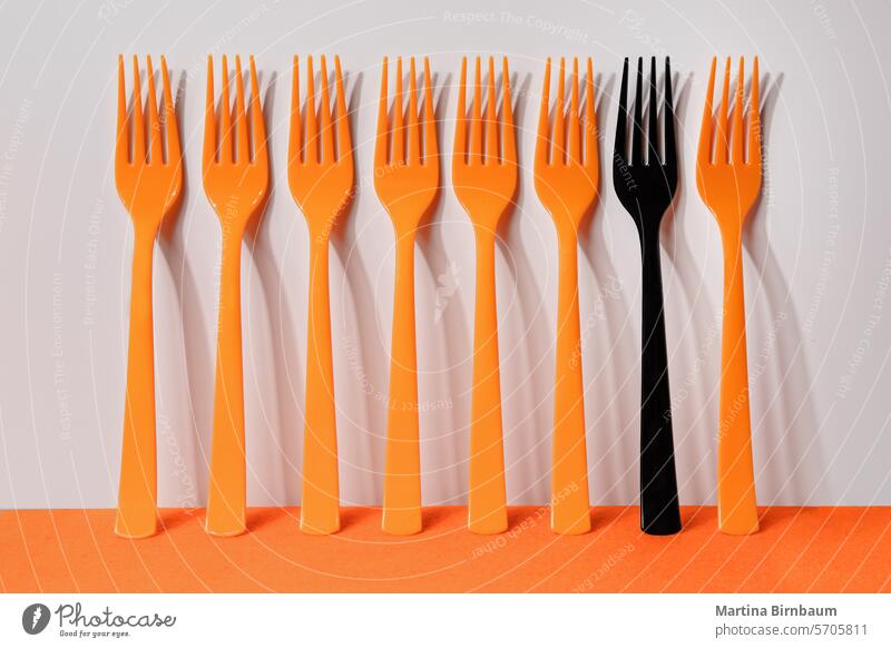 Sieben orangefarbene und eine schwarze Kunststoffgabel auf orangefarbenem und weißem Hintergrund Gabel Mahlzeit essen Löffel einfach Besteck Utensilien blau