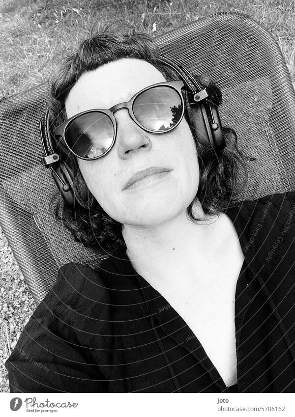 Frau entspannt mit Sonnenbrille und Kopfhörern auf einer Liege im Garten entspannung liegen Liegestuhl Urlaub Freizeit & Hobby Erholung Musik hören