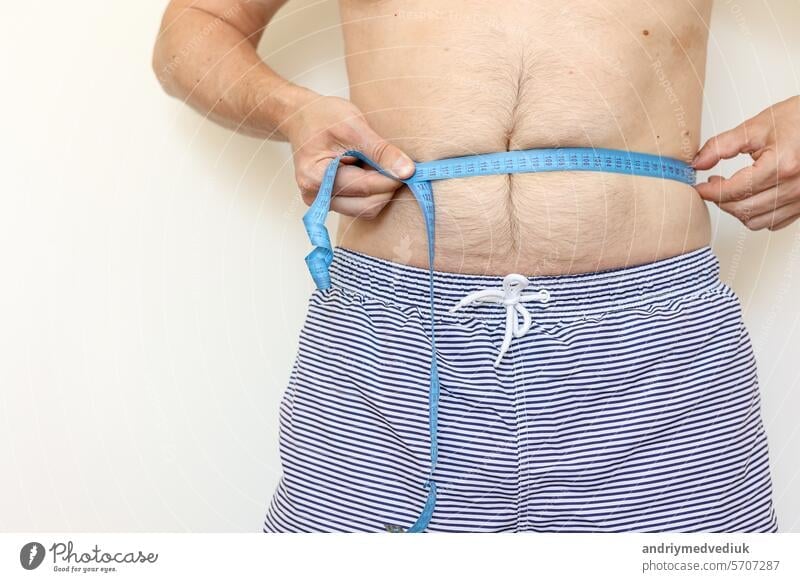 Mann misst seinen dicken Bauch mit einem Maßband und zeigt den Daumen nach oben. Konzept der Gewichtsabnahme, Gesundheitsprobleme von fettleibigen Menschen. Kontrolle des Essens und aktiver Lebensstil. Welt-Adipositas-Tag
