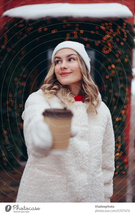 Frau in weißen Wollhandschuhen und Pelzmantel hält Kaffeebecher zum Mitnehmen im Freien Winter Halt Hand Fausthandschuh Tasse wegnehmen Nahaufnahme Wolle Mode