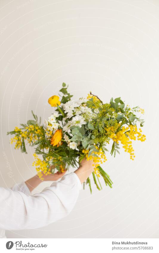 Hand hält schönen Strauß mit gelben Mimosen Frühlingsblumen, Ranunkeln und Eukalyptusblätter. Frische elegante Heimdekoration. Florist Arbeit. Blumen
