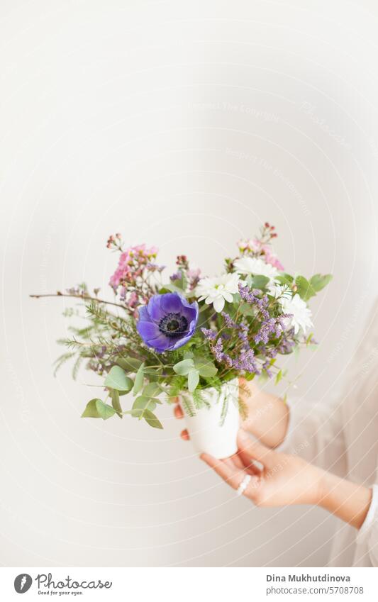 Hände halten schönen minimalen Blumenstrauß mit Frühlingsblumen. Lila Anemone und Eukalyptusblätter. Frische elegante Wohnkultur. Florist Arbeit. Salon Vase