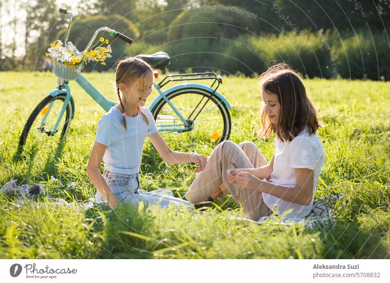 Zwei Teenager-Mädchen verbringen Zeit auf grünem Rasen im Park, flechten Zöpfe und Schwänze für einander, genießen Sommer und Ferien attraktiv Schönheit Fahrrad