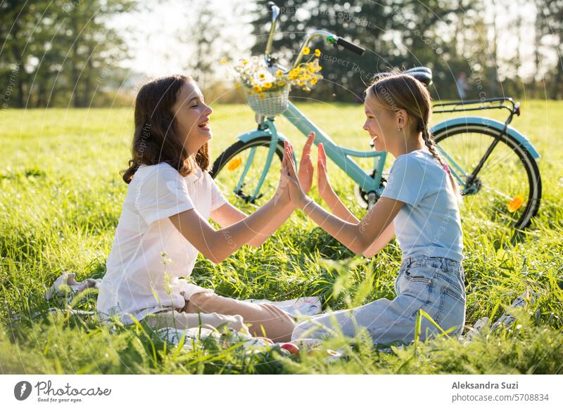 Zwei Teenager-Mädchen verbringen Zeit auf grünem Rasen im Park, flechten Zöpfe und Schwänze für einander, genießen Sommer und Ferien attraktiv Schönheit Fahrrad