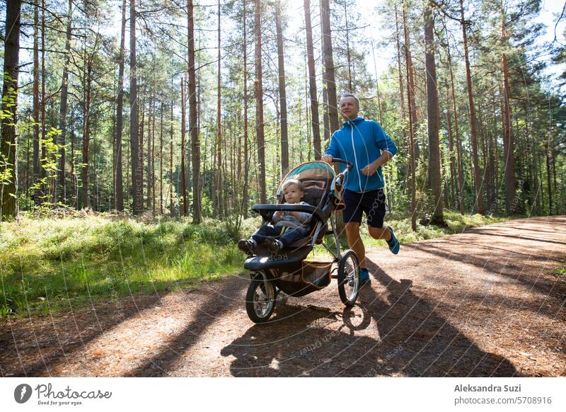 Sportlicher Mann in Sportkleidung läuft mit Kinderwagen an einem sonnigen Morgen im Stadtpark während der Vaterschaftszeit. aktiv Aktivität Erwachsener Herbst