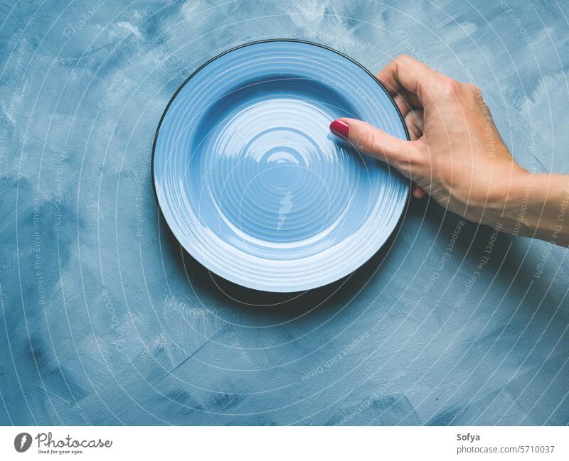 Blauer Hintergrund mit Teller und Frauenhand Hand nageln polnisch rot Keramik Geschirr Essgeschirr Speise essen Mittagessen Konzept Lebensmittel abstrakt leer