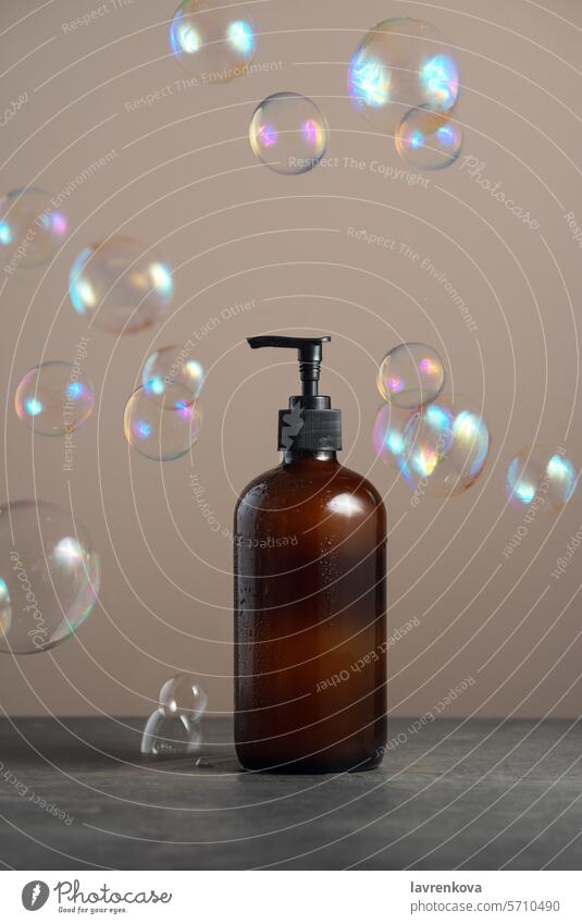 Umweltfreundlicher Braunglas-Seifenspender mit Pumpflasche, gefüllt mit Spülmittel oder Körperpflegemittel auf dunklem Marmorhintergrund mit Seifenblasen drum herum,