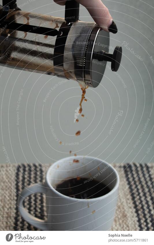 Einschenken von Kaffee aus einer Kaffeemaschine in eine weiße Tasse, vor einem gläsernen Hintergrund und einem gestreiften Tischset Kaffeetasse Frühstück
