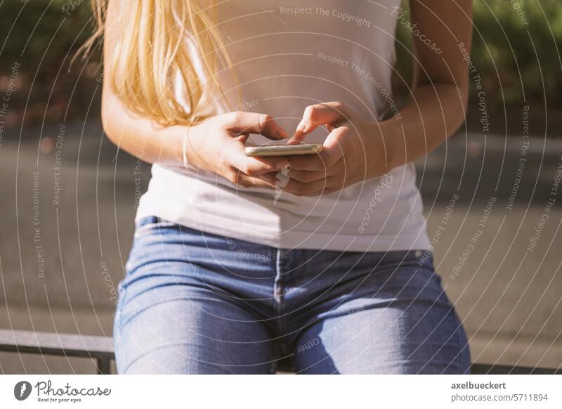 Junge Frau benutzt ein Smartphone an einem sonnigen Tag in der Stadt jung benutzend Mobile Telefon Texten Großstadt Nachrichtenübermittlung urban Nahaufnahme