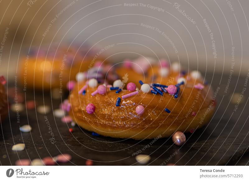 Großaufnahme von Donuts mit bunten Streuseln auf einer Wandtafel mehrfarbig Dessert süß Zucker Krapfen Glasur genießen Liebesperle Lebensmittel rund lecker