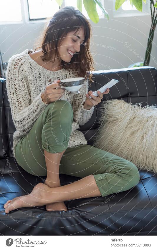 Eine fröhliche Frau auf einem Sofa mit einer Schüssel und einem Smartphone, die Komfort und modernes Leben verkörpert. freudig Schalen & Schüsseln lebend