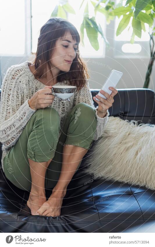 Ein gemütlicher Moment mit Kaffee und einem Smartphone. Frau Strickpulli Freizeit entspannt modern sonnenbeschienen friedlich Morgen Zeitgenosse lebend