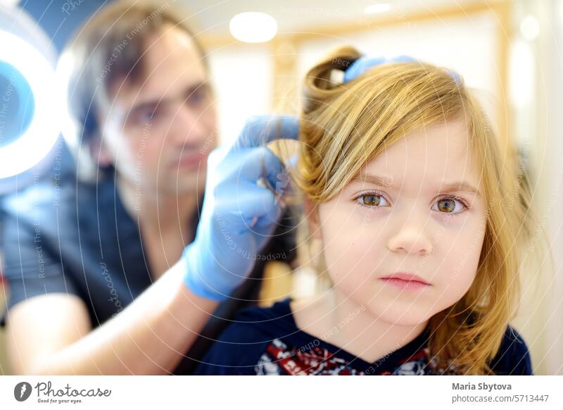 Nahaufnahme eines kleinen Mädchens bei einem Termin beim Dermatologen in einer modernen Klinik. Der Arzt untersucht die Haare und die Kopfhaut des Kindes auf Läuse und Nissen. Pedikulose ist eine häufige Krankheit bei Kindern