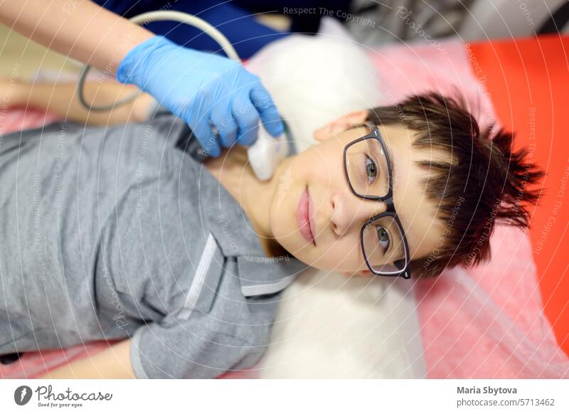 Arzt macht Ultraschall der Schilddrüse für Jungen mit Scanner-Maschine. Ärztin führt Ultraschallsensor über den Hals des Patienten zum Scannen der Schilddrüse und Lymphknoten.