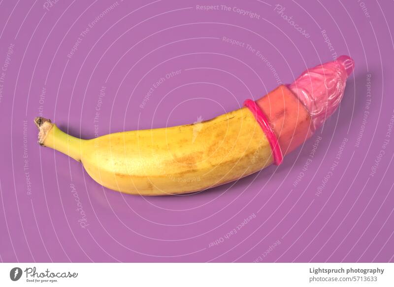 Rotes Kondom auf Banane mit lila Hintergrund. Safe Sex Konzept. Symbol Sexualerziehung sexuelle Fragen AIDS Verhütungsmittel Erektion