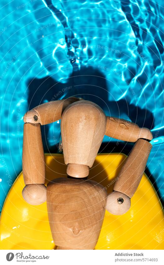 Eine hölzerne Künstlerpuppe, die auf einem gelben Schwimmkörper in einem schimmernden Pool liegt und die sommerliche Entspannung verkörpert Schaufensterpuppe