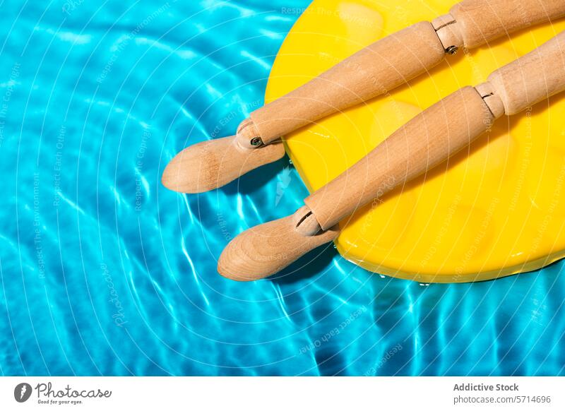 Körperteil einer hölzernen Schaufensterpuppe, die sich auf einem gelben Schwimmkörper im klaren blauen Wasser des Schwimmbads sonnt Pool Schwimmer Sonnenbad
