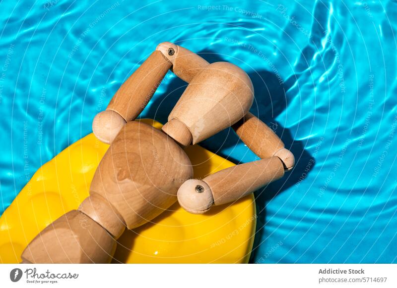 Hölzerne Künstlerpuppe, die sich auf einem gelben Schwimmkörper im klaren blauen Schwimmbadwasser entspannt und eine sommerliche Freizeitszene simuliert