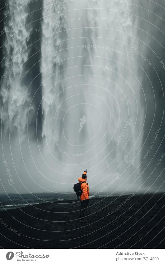 Unbekannter Mann in orangefarbener Jacke vor dem majestätischen Wasserfall Skogafoss Island reisen Nebel Abenteuer Natur im Freien männlich orange Jacke