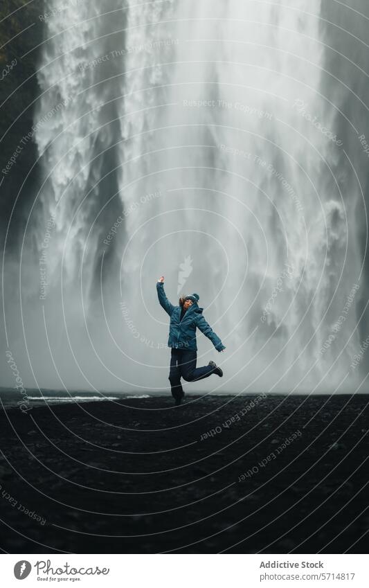Frau springt freudig vor einem majestätischen isländischen Wasserfall Island Reisender Freude springend Erkundung Abenteuer Natur kampfstark Hintergrund