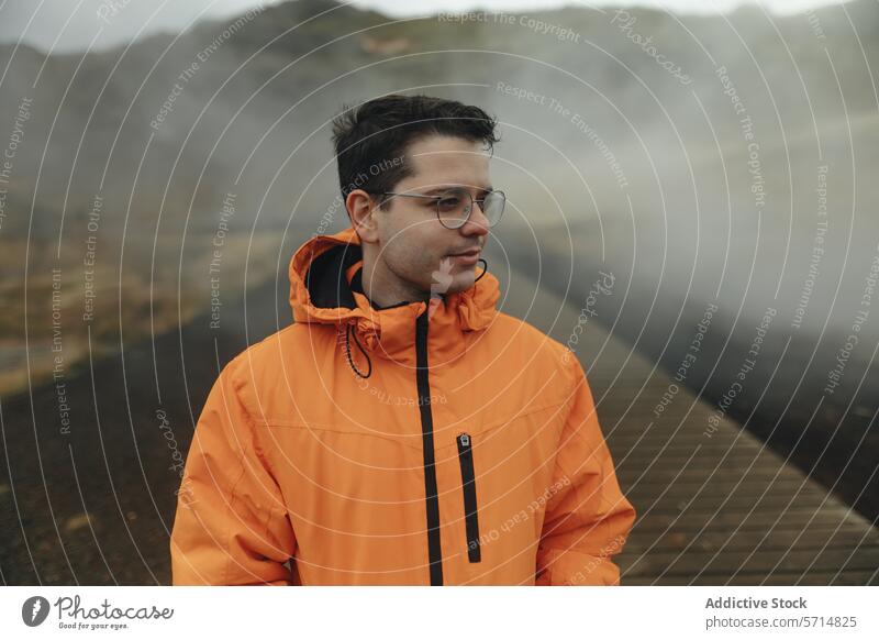 Mann in orangefarbener Jacke erkundet nebliges isländisches Terrain Island reisen Abenteuer männlich Regenmantel Nebel vulkanisch Landschaft im Freien Erkundung