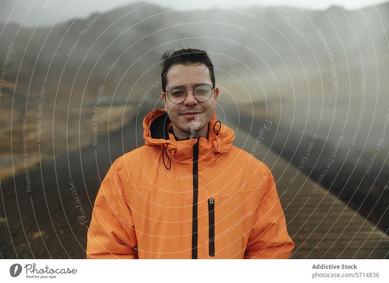 Mann in orangefarbener Jacke genießt neblige isländische Landschaft Island reisen Abenteuer männlich im Freien Nebel orange Jacke Lächeln Brille Promenade Natur