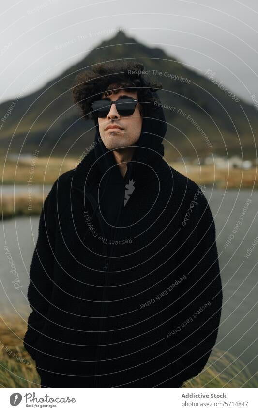 Mann in schwarzem Mantel vor isländischer Bergkulisse Island männlich Berge u. Gebirge Abenteuer Stil reisen im Freien Natur jung Sonnenbrille schwarzer Mantel