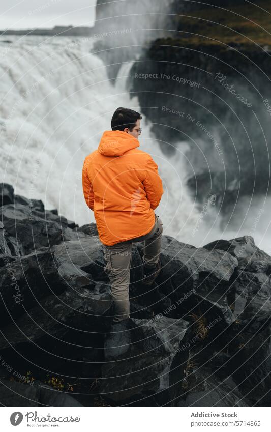 Anonymer Mann in leuchtend orangefarbener Jacke blickt auf den Gullfoss-Wasserfall, Island Reisender männlich orange Jacke Vulkangestein Natur im Freien