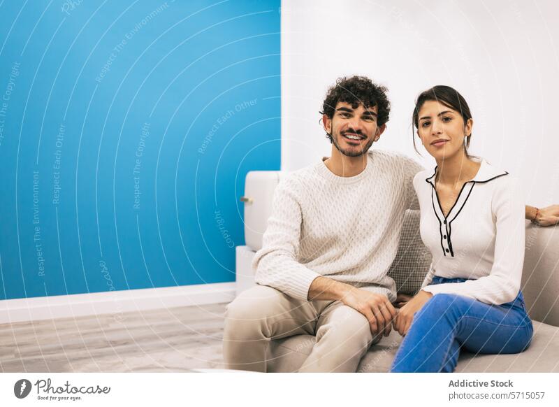 Lässiges Paar, das sich gemeinsam auf einem Sofa zu Hause entspannt heimwärts entspannend Komfort Lächeln posierend jung lässig gemütlich weiß Liege blau Wand