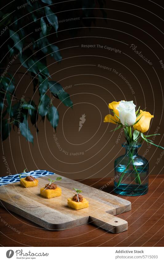 Elegantes Polenta-Häppchen mit Tomaten-Zwiebel-Eintopf Appetithäppchen schmoren hölzern Holzplatte Roséwein Vase gelb blau Hintergrund Amuse-Gueule