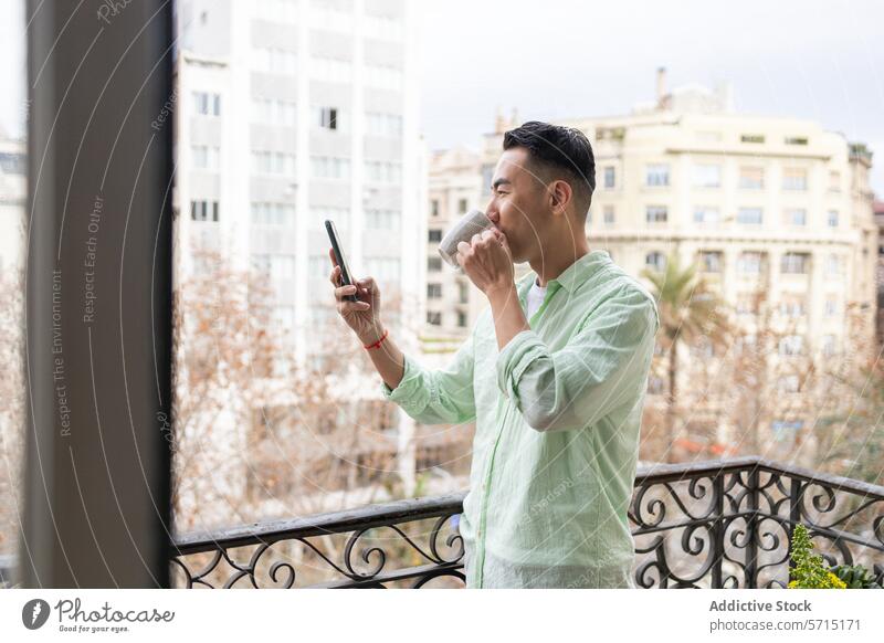 Asiatischer Mann genießt Kaffee und benutzt sein Smartphone auf dem Balkon asiatisch urban im Freien Tageslicht jung Erwachsener männlich Großstadt Freizeit