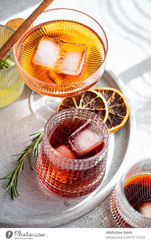 Eine Reihe erlesener alkoholischer Getränke in dekorativen Gläsern, begleitet von Eiswürfeln, einer Zimtstange, Rosmarin und getrockneten Zitrusscheiben auf einem marmorierten Tablett