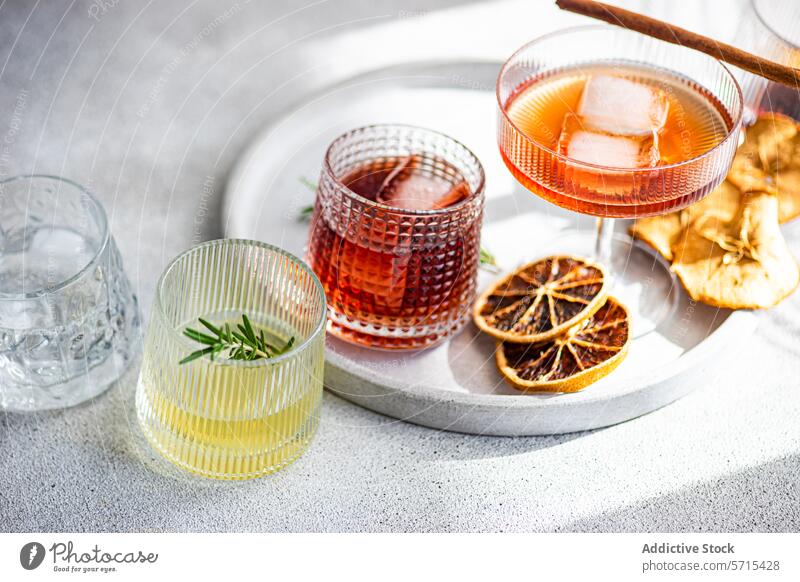 Eine vielfältige Sammlung von Spirituosen in gerippten Gläsern, darunter Kirschlikör mit Eis, Limoncello mit einem Rosmarinzweig und andere, die alle auf einem Tablett mit getrockneten Zitrusfrüchten liegen
